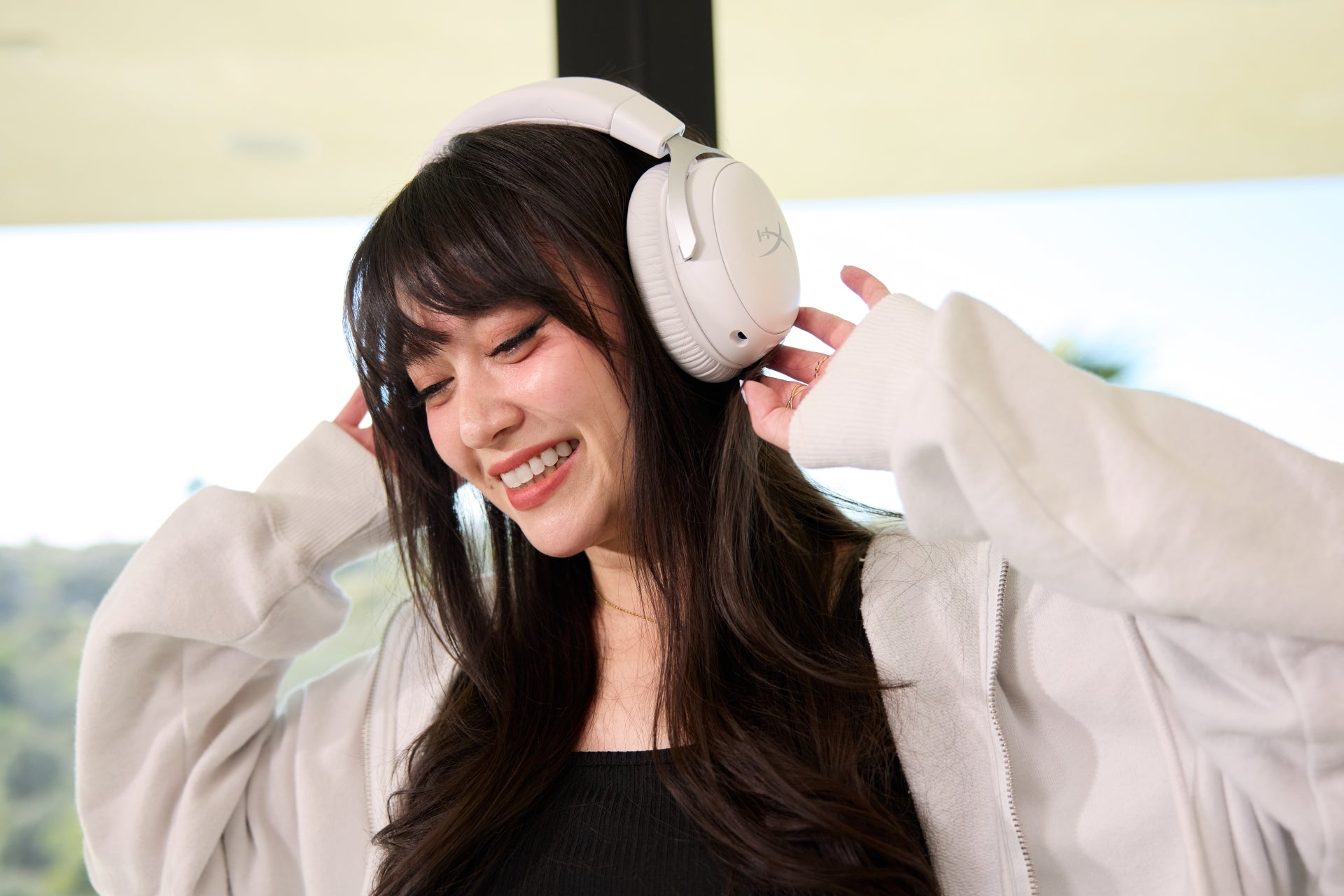 Woman wearing white gaming headphones and a light-colored coat indoors