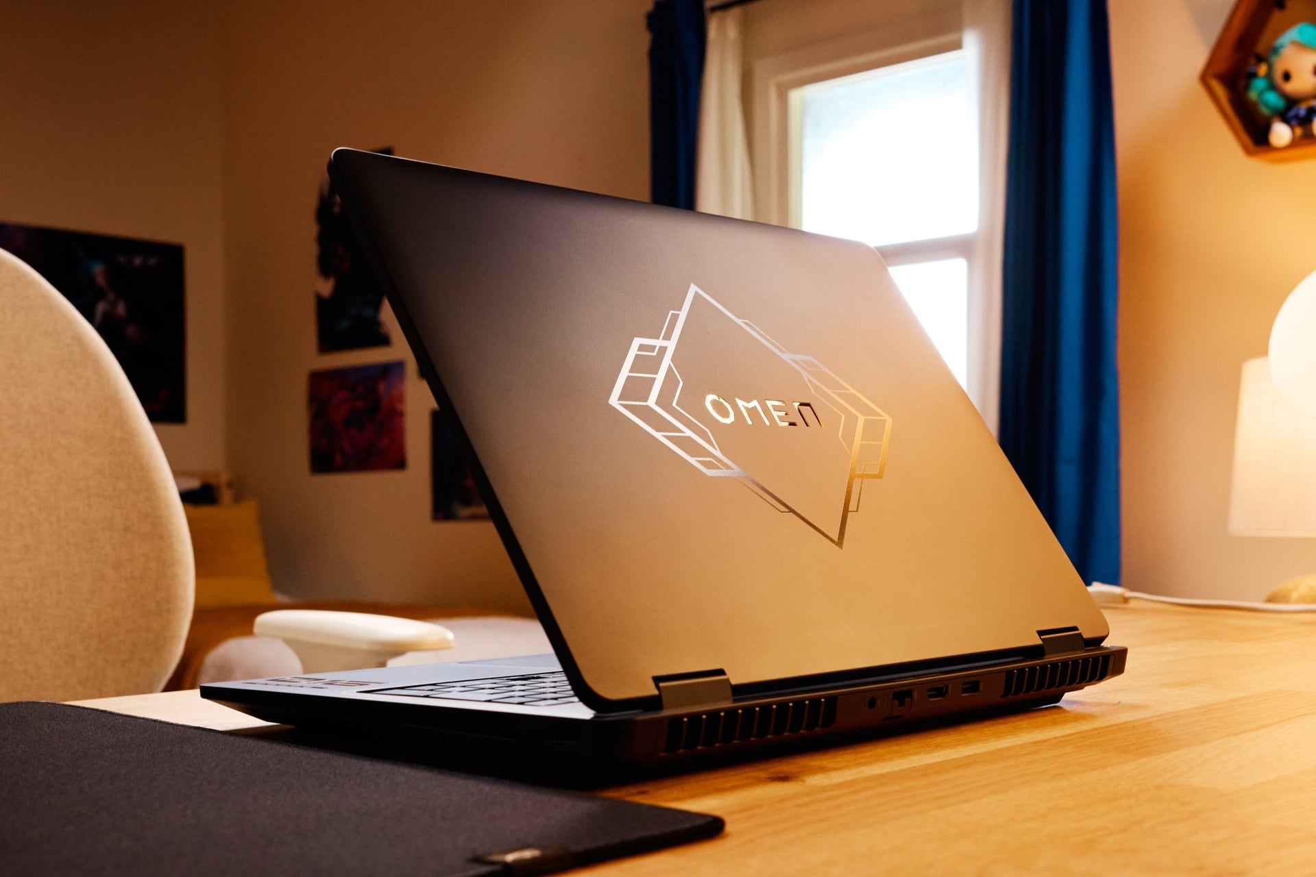 OMEN Laptop with gold accents on a desk in a room with a window and chair.